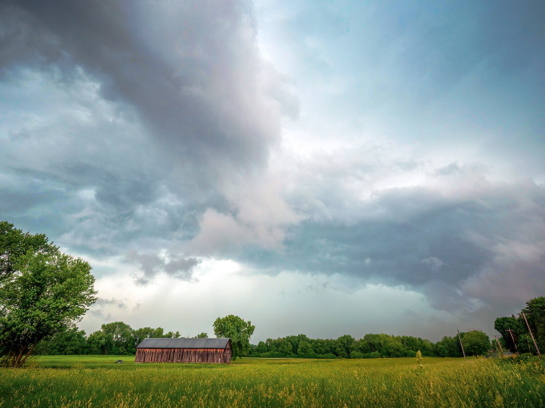 The shelf cloud from a line of strong storms, passing over some farmland in Western Massachusetts.⁠
⁠
Shelf clouds form along the edge of a thunderstorm’s outflow boundary, marking where the cold downdraft air from the storm meets the warm, humid surface air ahead of it. As the rain-cooled air descends and spreads out, it forces the warm surface air upwards. When this warmer air is lifted, it cools and condenses as it rises, forming the distinctive shelf-like arc along the leading edge of the gust front.⁠
⁠
I took this photo on a recent day in June, following severe storms moving through Massachusetts. I had just left the Berkshires after watching and photographing a supercell with a wall cloud. As I was trying to get to a good vantage point to watch the next closest storm, I passed this field and barn. Even though I was a bit closer to the storm than ideal (because of the rain), I had to stop to take this shot. I had all of about 30 seconds before the rain started to unload from above. Just enough time to setup my tripod, take a few photos (while constantly blowing water droplets off the lens), and then run out of there as the downpour hit. Very shortly after taking this photo, the wind and temperature shifted dramatically, as the outflow gust barreled through.