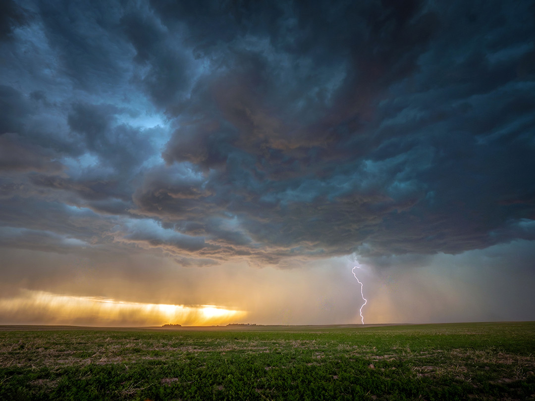 Lightning erupts from a powerful supercell as rain falls before the golden setting sun, above the plains of Nebraska.⁠
⁠
While storm chasing, the safest and most ideal location to view a storm is typically from the southeast, assuming a northeast-moving storm. This positioning, known as the “right flank,” gives you clear roads to escape the storm’s path and reduces the chances of encountering large hail or, of course, a tornado.⁠
⁠
Tornadoes most frequently occur in the late afternoon and early evening, so most storm chasing happens towards the end of the day. And since you're usually staying to the southeast of the storm, you're inevitably facing west, perfect for observing a passing supercell at sunset.⁠
⁠
Because these storms are often enormous, they tend to block the sunlight you'd otherwise see. But occasionally, breaks in the clouds allow sunset light to shine through, as it did this evening. Bands of rain fell in front of the glowing light, further enhancing its golden hue, while lightning struck repeatedly from the dramatic and powerful storm above.⁠
⁠
Taken on June 15th, 2025, in the southern Nebraska Panhandle.