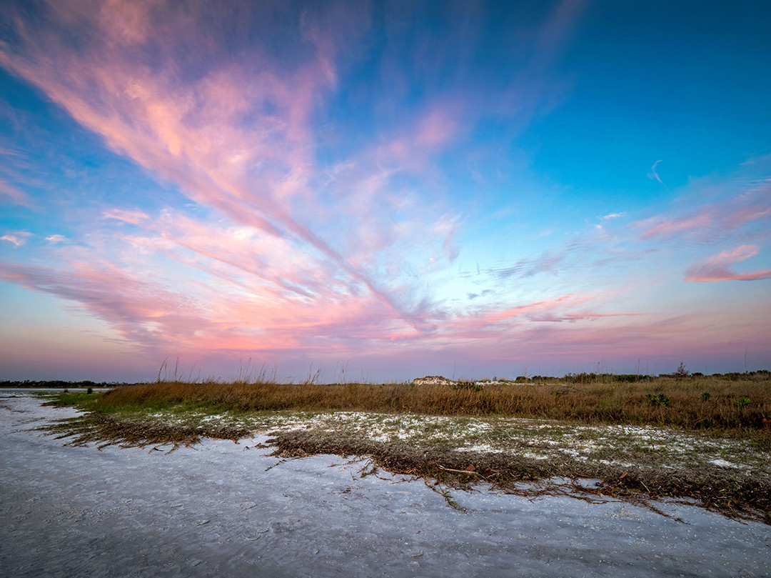 Pastel sunset colors fan across the sky over the white sands of Fort De Soto Park, Florida.⁠
⁠
A month ago, I spent a few days in the Tampa area, on the Gulf Coast of Florida. When I know I will be photographing an array of sunsets, I use an app on my phone to identify which locations (and dates) have the highest probability of color in the sky during sunset, using live weather data. My original plan after landing this afternoon was to go to the Palm Harbor area, as I was staying nearby, and the original forecast had that area being ideal for color.⁠
⁠
But once my plane landed, I connected to that app again, and things had shifted a bit. Now the St. Petersburg area (about an hour further south) was forecasted to have significantly higher color potential than Palm Harbor. So, I shifted my plans, grabbed my rental car, and headed straight for Fort De Soto Park, one of the more visually stunning beaches in that region, and in the center of this color forecast.⁠
⁠
What I didn’t realize is that this park closes at sunset. Which, in all fairness, I did see the signs proclaiming this as I drove in, but I figured there was a bit of a buffer in terms of the adherence of this policy, and I would have a good 15 minutes or so to take my photographs after the sun dropped behind the horizon.⁠
⁠
So, to my surprise, as I adjusted and relocated my tripod based on which parts of the sky had the best color, a park ranger drove her truck up to me (literally about 30 seconds after the sun set), alerting me that they were now closed, and that I must leave. I took an extra ten seconds in this moment to take this photograph, packed up, and made my way back to my car.