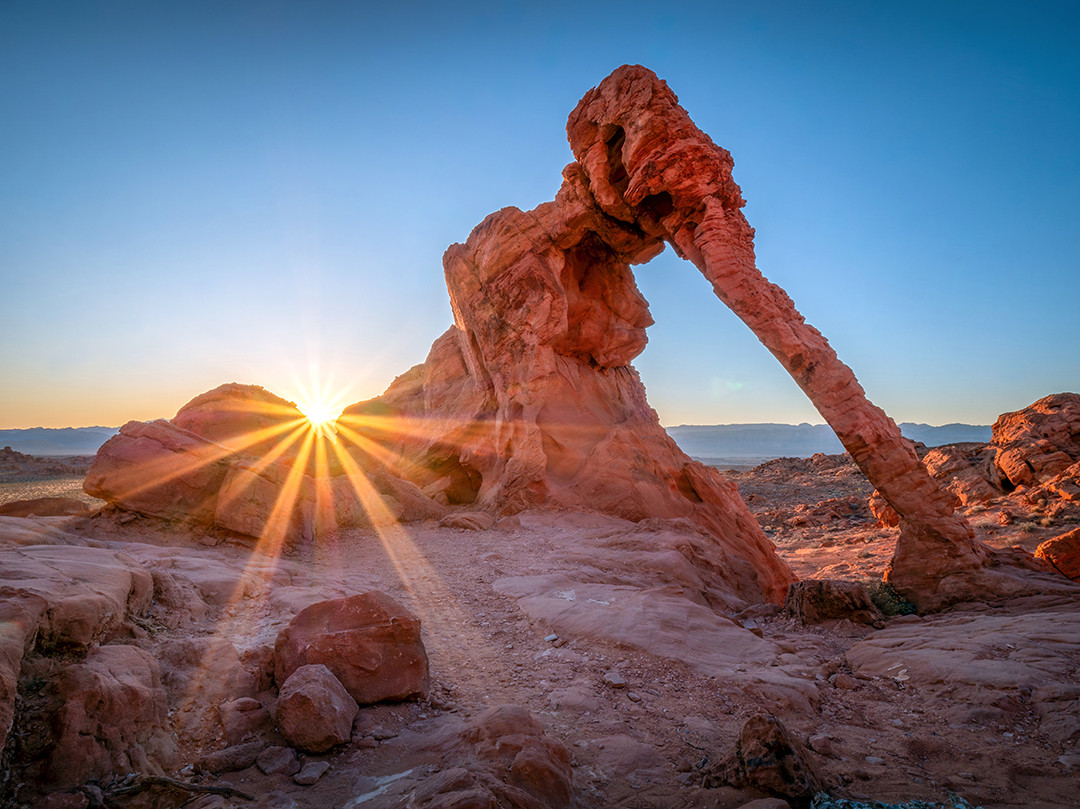 The rising sun peeks behind Elephant Rock in Valley of Fire State Park, Nevada.⁠
⁠
Natural sandstone arches are some of my favorite subjects to photograph, and they come in a wide variety of shapes, sizes, colors, and levels of accessibility. This is definitely one of the more uniquely shaped arches I have photographed, with its delicate appearance almost seeming to defy physics. Named Elephant Rock for obvious reasons, its shape and distinctive “trunk” were created over millions of years through the weathering and erosion of the Aztec Sandstone from which it is formed.⁠
⁠
When standing before it, it feels like one of those arches that surely cannot remain standing for much longer, simply because of how thin the trunk is and how much weight it appears to be supporting. Thankfully, the climate in Valley of Fire is well suited to preserving formations like this. With minimal vegetation and infrequent rainfall, erosion occurs slowly, allowing delicate rock structures such as Elephant Rock to persist for thousands of years.⁠
⁠
I took this photograph at the tail end of a recent trip to Arizona, stopping here in Nevada before heading to the airport that morning. Valley of Fire is about an hour outside of Las Vegas, and Elephant Rock is only about a five-minute walk from the park entrance, making this an easy sunrise location to photograph. It allowed me to sneak in one last image before departing on my flight.