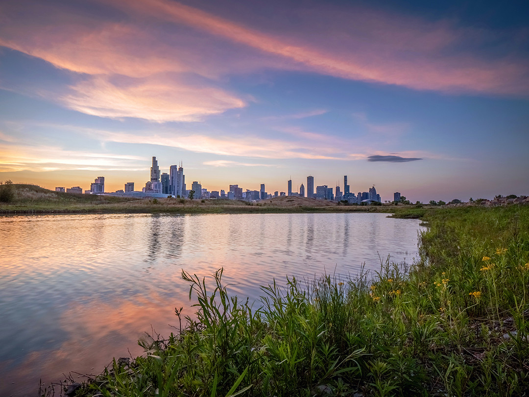 The Chicago skyline at sunset, seen from the lagoon at Northerly Island Park.⁠
⁠
I am fortunate enough to visit the Chicago area on a semi-regular basis, and have photographed the skyline during a handful of those visits. Northerly Island is a unique area because it is a former airfield that was transformed into an urban nature preserve. Merrill C. Meigs Field was the busiest single-strip airport in the United States and a major hub for Chicago’s business elites and politicians. Its destruction was controversial at the time, as the mayor ordered its bulldozing to begin in the middle of the night, keeping it a secret from the aviation community, and everyone else, really.⁠
⁠
Citing the security concerns of having such busy air traffic so close to the skyscrapers of downtown Chicago, it was decided that reclaiming this strip of land for parkland would be more beneficial to the people of Chicago as a whole.⁠
⁠
Covering around 100 acres, this park features a 5-acre pond, native prairies, savannas, and a hiking trail circling the lagoon, all while enjoying beautiful views of Lake Michigan and the Chicago skyline. While almost all of my previous skyline photographs included urban surroundings, Northerly Island provides a rare combination of natural foregrounds mixed with manmade backgrounds. The reflections in this lagoon complemented the skyline, as well as the setting sun’s pastel pink hues.