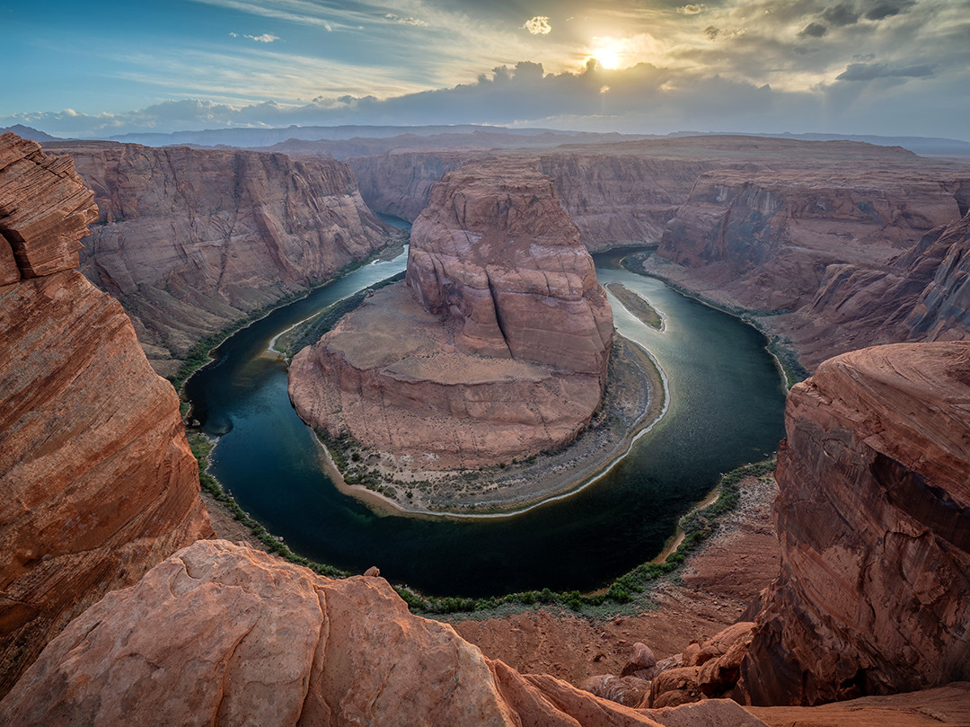 The Colorado River makes a U-turn as the sun sets behind Horseshoe Bend at the end of a windy day in Page, Arizona.⁠
⁠
This area of Glen Canyon is where the Colorado River makes its approximately 270-degree turn, creating the aptly named Horseshoe Bend. The rim of the canyon here sits roughly 1,000 feet (305 m) above the river, making the scale of this massive bend difficult to fully capture in a photograph.⁠
⁠
What is likely the most beautiful and well-known location in Page, I knew I wanted to spend at least one evening here capturing the sunset, which would turn out to be more difficult than I expected. I ended up going three nights in a row, with all three having either complete or partial cloud cover. In addition to the clouds, the wind proved to be a bigger opponent to my photography than I anticipated. This overlook is extremely exposed, with almost no vegetation or surrounding terrain to provide shelter, leaving you to experience the full force of the high desert wind when it picks up. As if standing on the edge of a 1,000-foot cliff isn’t nerve-wracking enough, adding strong, sandblasting gusts on top of it only adds to the excitement.