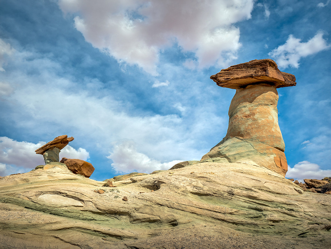 Two large mushroom hoodoos rise from a cross-bedded sandstone base beneath a sky filled with cumulus clouds in northern Arizona.⁠
⁠
What was probably my favorite place to photograph during my brief trip to Page, Arizona, Stud Horse Point is an area that sits on a mesa near the Arizona-Utah border, where a concentration of these unique hoodoo formations can be found.⁠
⁠
Much of the sandstone here is cross-bedded, a feature created when layers of sand were deposited at angles along the slopes of ancient dunes before eventually becoming solid rock. Those layers remain visible today as sweeping bands through the sandstone, preserving evidence of the direction and movement of sediment across this ancient landscape.⁠
⁠
The hoodoos themselves form through differential erosion, where a harder layer of caprock resists weathering better than the softer material beneath it. As the surrounding rock gradually erodes away, the caprock acts somewhat like a stone umbrella, slowing the erosion of the narrower pedestal directly below it and helping preserve the distinctive mushroom-shaped formation.
