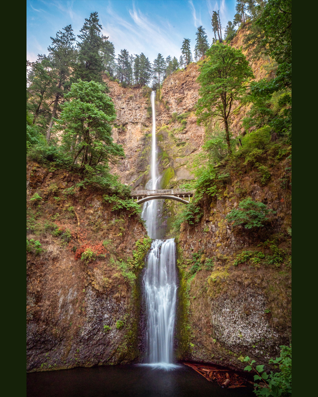 The two-tiered Multnomah Falls plunges down behind the Benson Footbridge within the Columbia River Gorge in Oregon.⁠
⁠
Considered the most famous waterfall in the Pacific Northwest, Multnomah Falls drops a total of 620 feet (189 m), with the upper tier falling 542 feet (165 m) and the lower tier another 69 feet (21 m). The Benson Footbridge, part of the Multnomah Falls Trail, also known as the Larch Mountain Trail (#411), sits roughly halfway up the waterfall and provides an up-close view of the midpoint of this spectacular natural wonder.⁠
⁠
Over 2.5 million visitors come to this site each year, making it the most visited natural attraction in Oregon and one of the most popular waterfalls in the United States by visitor count. Given this, it is easy to understand why timed permit reservations are required during the summer months, as the demand to witness its beauty is immense.⁠
⁠
That is part of the reason I arrived incredibly early on this day, just as the sun began to rise, early enough to avoid the need for a permit and the Disney World sized crowds that soon follow. Experiencing this majestic waterfall in peace completely transforms the atmosphere and allows its serenity to truly shine.