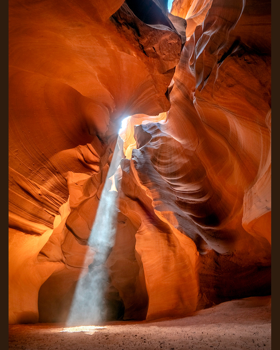 A shaft of sunlight illuminates the sculpted sandstone walls of Upper Antelope Canyon in the Navajo Nation, Arizona.⁠
⁠
Upper Antelope Canyon is carved into Navajo Sandstone, a rock formation that originated roughly 190-200 million years ago during the Jurassic Period, when this region was covered by an immense field of desert sand dunes. Over time, those dunes were buried and eventually lithified into stone. The canyon itself was carved primarily by flash flooding, with floodwaters spiraling, accelerating, and changing direction as they moved through the narrow sandstone passages.⁠
⁠
The tall, narrow nature of the canyon creates the light beams for which it is most famous, as seen in this photograph. These beams are especially visible on windier days, when airborne sand and dust scatter the sunlight, making the shafts of light appear almost solid as they shine through openings high above the canyon floor. The effect is strongest around midday, when the sun is positioned high enough in the sky for its light to penetrate directly into the canyon.⁠
⁠
Upper Antelope Canyon is a slot canyon within the Navajo Nation, just outside of Page, Arizona. This region is rich in, and famous for, its slot canyons, most notably Upper and Lower Antelope Canyon. They are both incredibly beautiful, but also heavily visited. Taking a tour through this wonder of nature allows you to experience its beauty up close, but it also means sharing the canyon with the thousands of other visitors who pass through it each day. During peak season, Upper Antelope Canyon can host anywhere from 3,000 to 10,000 people per day. I am still very happy and fortunate to have witnessed such beauty firsthand, but numbers like that can blur the line between natural wonder and tourist attraction.