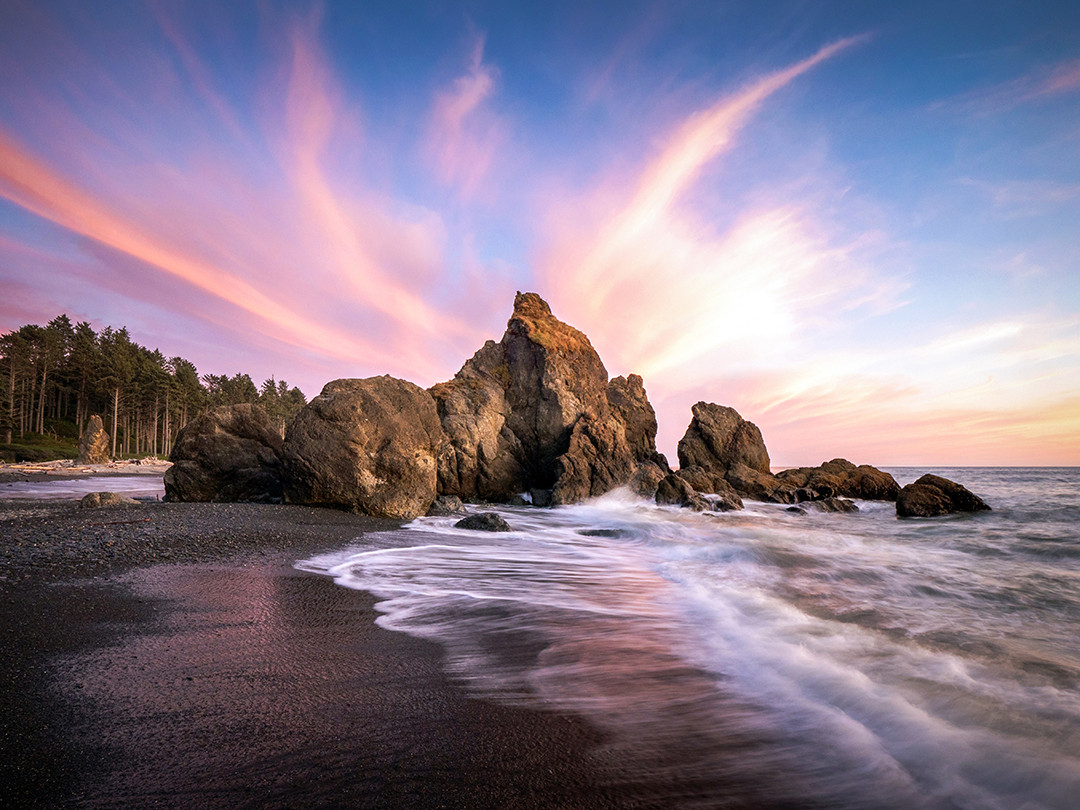 Wispy cirrus clouds painted by the setting sun radiate above a large set of sea stacks, as the waves crash upon Ruby Beach, inside Olympic National Park in Washington.⁠
⁠
Last month, I posted a photo of the sun setting behind a few sea stacks in this exact location at Ruby Beach, in Olympic National Park. That photo was taken just five minutes prior to this one, and was the entire reason why I ventured down to this beach in the first place. I had that specific shot in mind, and ultimately got what I was after.⁠
⁠
But sometimes, if you happen to be in the right place at the right time, better opportunities just happen to present themselves. After the sun had set, I noticed this wispy cluster of cirrus clouds start to be illuminated by the recently set sun. It was not centered over the rocks the way it is in this photo, I had to move a few hundred feet to make that happen, ultimately standing, with my tripod, in a couple of feet of water to do so. Distracted by the task of taking this photograph and capturing the waves’ motions, I was caught blindsided by an incoming rogue wave, which nailed both me and my tripod with force, spraying my camera in the process. Knowing how damaging salt water can be to electronics, I quickly ran back onto the beach, drying everything as quickly as possible. Luckily, everything survived the ordeal, but if you are going to stand in the powerful Pacific Ocean, do know that rogue waves occur regularly and can take you and your equipment out in a moment.